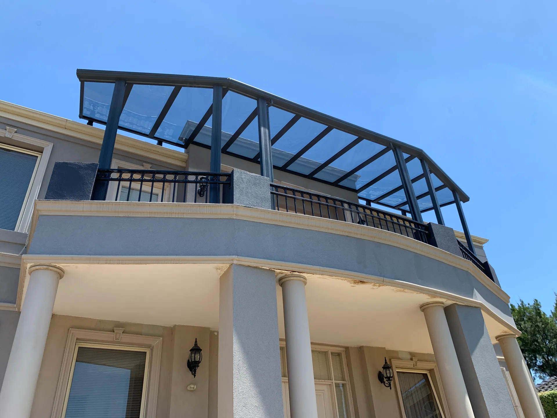 Upper-level transparent patio roof following the changing line of a curved residential façade